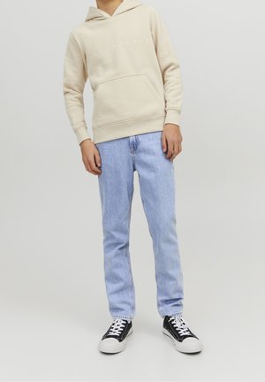 Sweatshirt beige à capuche avec poche avant, jeans bleu clair et baskets noires avec semelles et lacets blancs. Tissu lisse, décontracté et léger.