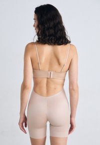Lenjerie shapewear nudă, fără cusături, cu un sutien cu bretele ajustabile și un fund înalt care se extinde până la mijlocul coapsei. Textură moale și netedă.