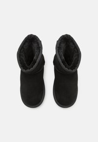 Botines de ante negros con un forro suave y esponjoso, que presentan una puntera redondeada y un diseño de puño doblado. Suelas de goma planas.