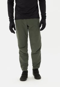 Groene outdoorbroek van lichtgewicht materiaal, met een rechte pasvorm en minimale details, gecombineerd met zwarte laarzen en handschoenen.