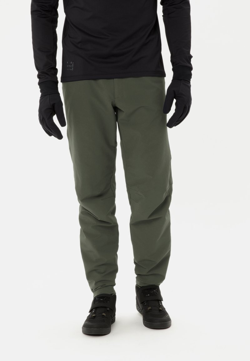 Groene outdoorbroek van lichtgewicht materiaal, met een rechte pasvorm en minimale details, gecombineerd met zwarte laarzen en handschoenen.