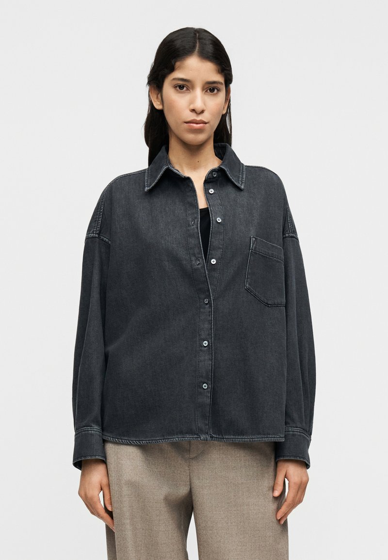 Σκούρο πουκάμισο από τζιν με κουμπιά, γιακά, μία τσέπη στο στήθος και άνετη εφαρμογή. Διαθέτει ραφές σε αντίθεση και κλείσιμο με κουμπιά.