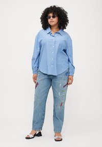 Blå og hvitstripet skjorte med lange ermer, kombinert med lyseblå jeans med fargerike malingssøl. Flate sandaler.