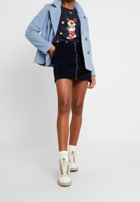 Ljusblå ylleblandad kappa, marinblå grafisk t-shirt med renmotiv, svart corduroy mini kjol med framdragkedja, vita ankel sneakers.