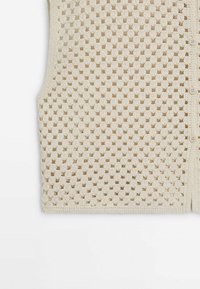 Strickweste in hellem Beige mit offenem Gewebe und kreisförmigen Mustern, einem runden Ausschnitt und einem Knopfverschluss auf der rechten Seite.