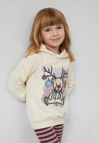 Kremowa bluza z kapturem z graficznym wzorem renifera i ozdobami. Połączona z bordowymi legginsami w biały prążek. Miękka tkanina, luźny krój.
