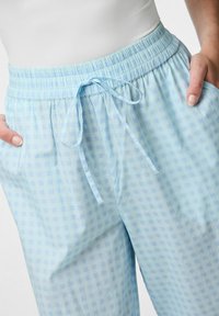 Lichtblauwe geruite broek van zachte stof, met een elastische tailleband en een koordje. Het patroon is een subtiele lichtblauwe structuur.