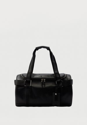 Čierna kožená taška typu duffel s dvoma rukoväťami, horným zipsom na zatváranie, bočnými popruhmi a pripevnenou obdĺžnikovou visačkou na batožinu na jednoduchom pozadí.