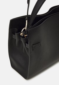 Black textured leather tote bag with double handles and gold-toned hardware on a white background, showing structured side and interior.