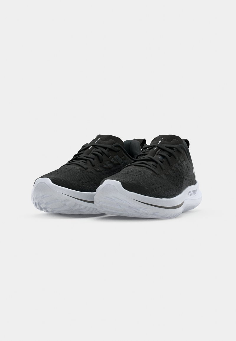 Schwarze Sport Schuhe mit einem strukturierten Strick-Obermaterial, ausgestattet mit einer weißen Mittelsohle und Gummisohle, akzentuiert durch minimale Markenkennzeichnung und Schnürsenkel.