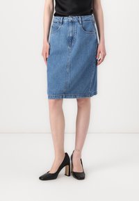 Gonna midi in denim blu con taglio dritto, tasche frontali e orlo che arriva appena sopra il ginocchio, abbinata a scarpe con tacco alto nere.