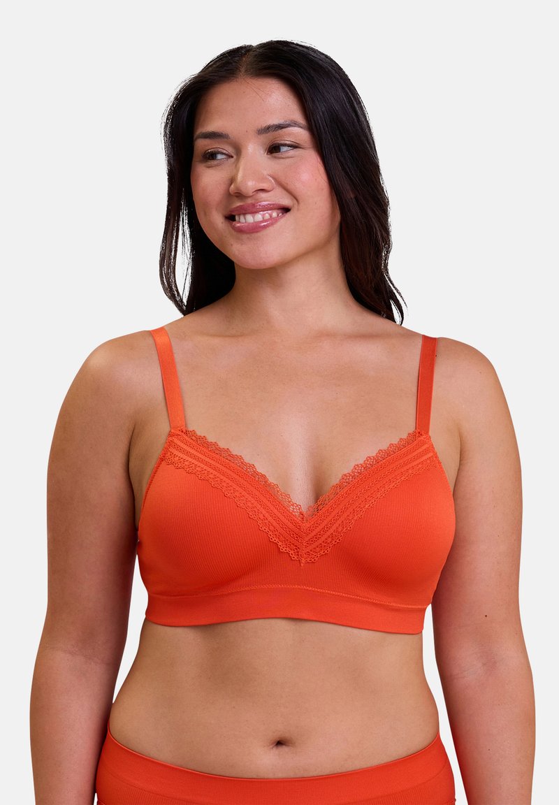 Oranje geribbelde bralette met kantafwerking langs de v-hals, verstelbare bandjes en zachte stof voor comfort. Bijpassende onderkleding zichtbaar.