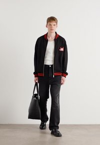 Black zip-up bomber jacket with red accents, white t-shirt, black jeans, and black shoes. Carrying a soft, black tote bag.