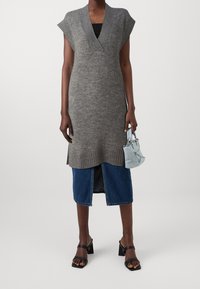 Abito grigio lavorato a maglia con scollo a V, maniche corte e dettagli a coste. Abbinato a una gonna di jeans e una borsa a tracolla blu chiaro. Sandali neri con tacco a blocco.