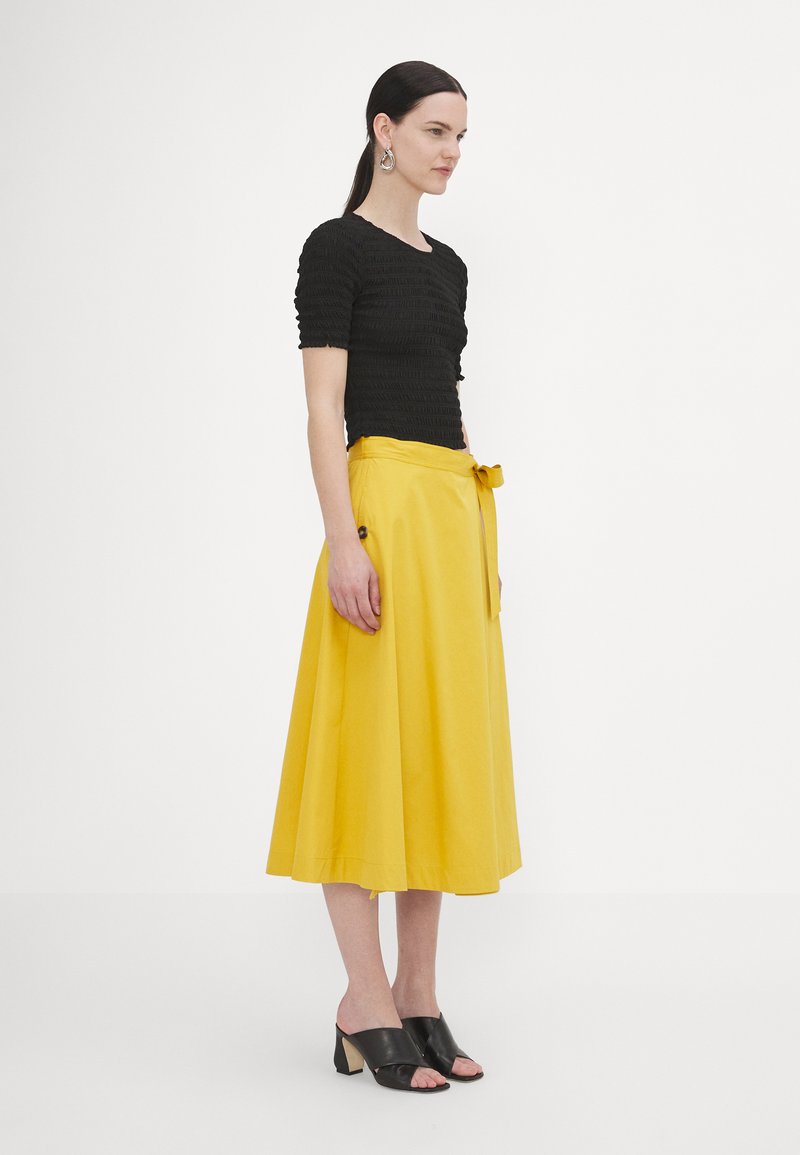 Black, ribbed top with short sleeves; yellow, A-line skirt with a waist tie; black open-toe mules with a block heel.
