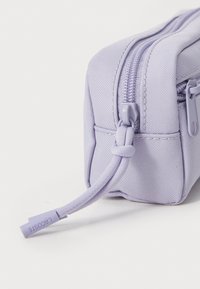 Trousse à crayons en tissu violet avec une surface texturée, de forme rectangulaire, deux fermetures à glissière lisses et une languette de tirage nouée. Branding minimal visible.