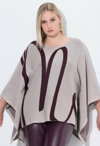 Poncho beige con un diseño abstracto en burdeos, hecho de punto suave. Presenta mangas anchas y un corte holgado, combinado con pantalones burdeos oscuros.