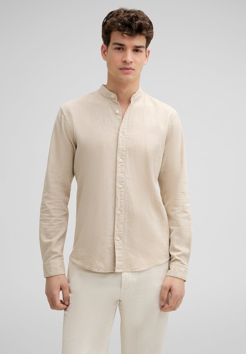 Beige overhemd met lange mouwen en een mandarinakraag, met een subtiele textuur en knoopsluiting. Draagt men met lichtgekleurde broek.