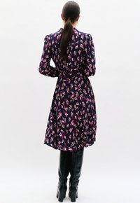 Robe marine avec un motif de feuilles roses et blanches ; manches longues, taille cintrée, jupe évasée. Associée à des bottes noires jusqu'aux genoux.