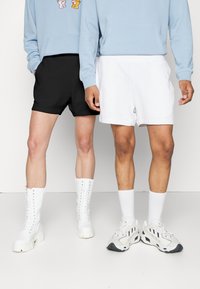 Svarte og hvite shorts med elastiske midjebånd. Ett par er svarte, og det andre er hvitt. Begge har forskjellige stiler sko.