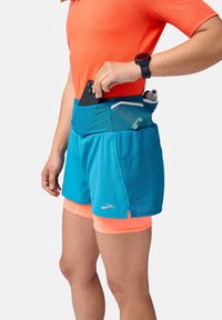 Shorts de sport bleus avec une taille en mesh, comportant des poches qui contiennent un téléphone et une bouteille d'eau. Le haut est orange vif, fabriqué dans un tissu léger.