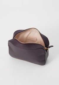 Purple leather pouch with a textured finish, gold zipper, and a light pink interior. The interior features a brand label.