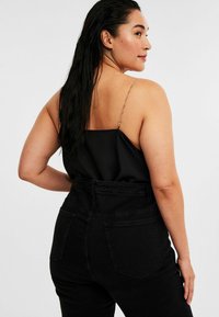 Svart satin linne med tunna kedjestraps; parat med högmidjade svarta denimjeans med bakfickor och en texturerad yta.