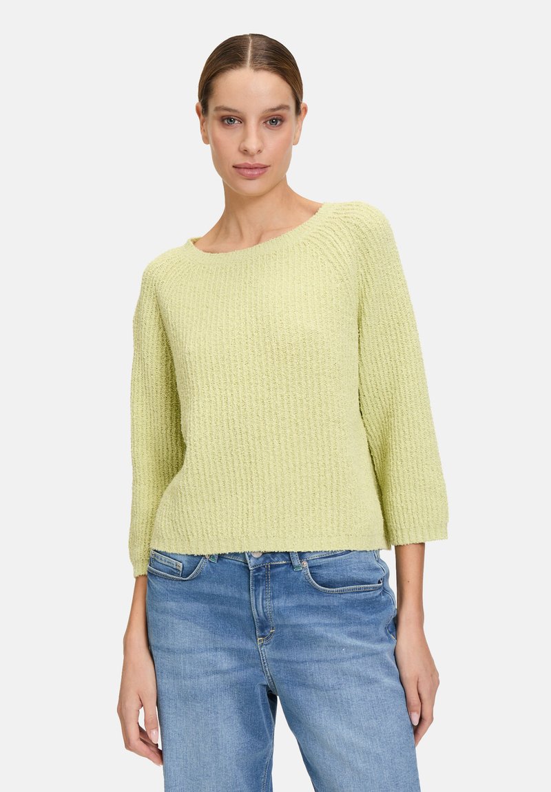 Hellgrüner strukturierter Pullover mit Rundhalsausschnitt und Dreiviertelärmeln, kombiniert mit blauen Jeans.