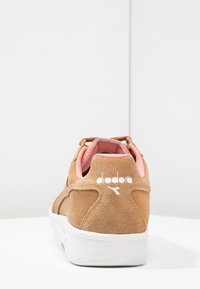 Semišové tenisky v béžové barvě s růžovými akcenty, s bílou gumovou podrážkou a logem na patě. Měkká textura s zaobleným designem.
