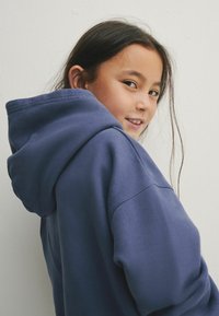 Sudadera con capucha de color azul marino con una textura suave y un ajuste holgado, que cuenta con un cordón en la capucha y costuras de hombros caídas.