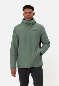 Giacca impermeabile verde con colletto alto, zip frontale e tasche laterali. Presenta polsini elastici e un logo discreto sul lato sinistro del petto.