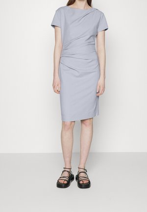 Kobieta ubrana w jasnoniebieską sukienkę do kolan z krótkimi rękawami oraz czarne sandały na platformie z cienkimi paskami.