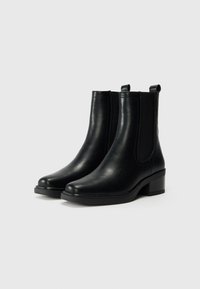Bottines en cuir noir avec panneaux élastiques sur les côtés, bout rond et petit talon bloc. Présente des accents de couture le long des côtés.