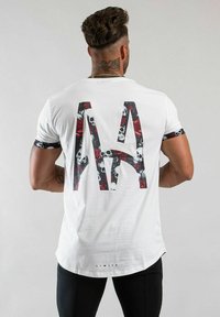 Vit t-shirt med en stor "MA" grafik på baksidan, som har döskallar och röda rosor; svart accent på ärmarna. Mjukt tyg, böjd nederkant.
