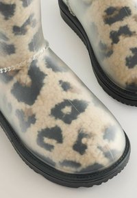 Permatomi kulkšnies batai, turintys smėlio ir juodo leopardų rašto dizainą, pagaminti iš gumos, su tekstūruota paviršiumi ir juodu padu.