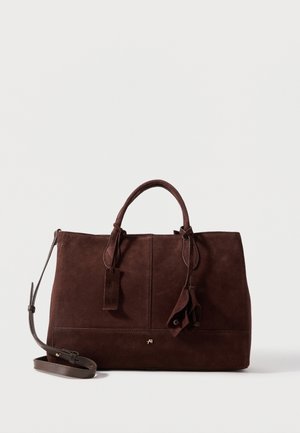 Donkerbruine suède handtas met dubbele hengsels, afneembare schouderband, gestikte details en decoratieve leren kwastjes op een witte achtergrond.