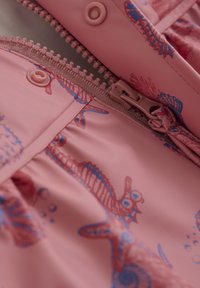 Rosa regnjacka med dragkedja, prydd med illustrationer av sjöhästar och snäckor i blått och rött. Tillverkad av hållbart, vattenavvisande material.