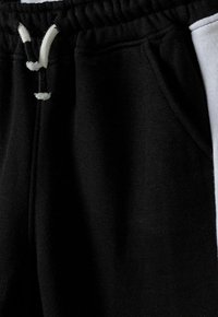 Zwarte sweatpants met een trekkoord in de taille, voorzien van een zijzak en een contrasterend grijs paneel. Zacht, textured stof met een sportief ontwerp.