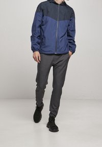 Marinblå huvjacka med en kontrasterande mörkare övre sektion, ihop med grå avsmalnande byxor och svarta sneakers.