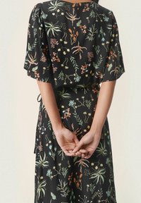 Abito nero a fiori con maniche corte, una vestibilità rilassata e intricati motivi botanici in tonalità di verde, arancione e giallo.
