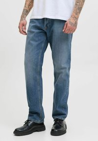 Tunnade blå jeans i en avslappnad passform, med rak skärning, i kombination med svarta läderskor och en vit t-shirt, som visar enkel stil.