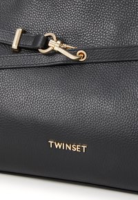 Sort tekstureret lædertaske med en guldfarvet hardware-lås og et "TWNSET" logo i guld nederst. Glat overflade, kompakt design.