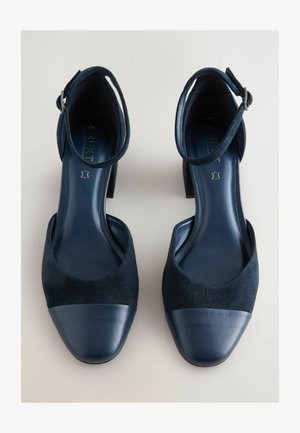 Scarpe col tacco nere in camoscio con una tomaia in camoscio e una punta in pelle liscia; presentano un cinturino alla caviglia con una fibbia argentata.