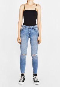 Svart kroppsnära bodysuit med tunna band, ihop med ljusblå skinny jeans med slitna knän, och svarta sneakers med vita snören.