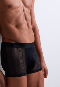 Boxers noirs à motifs avec une taille élastique douce. Le tissu est semi-transparent, mettant en valeur un design géométrique et une coupe ajustée.