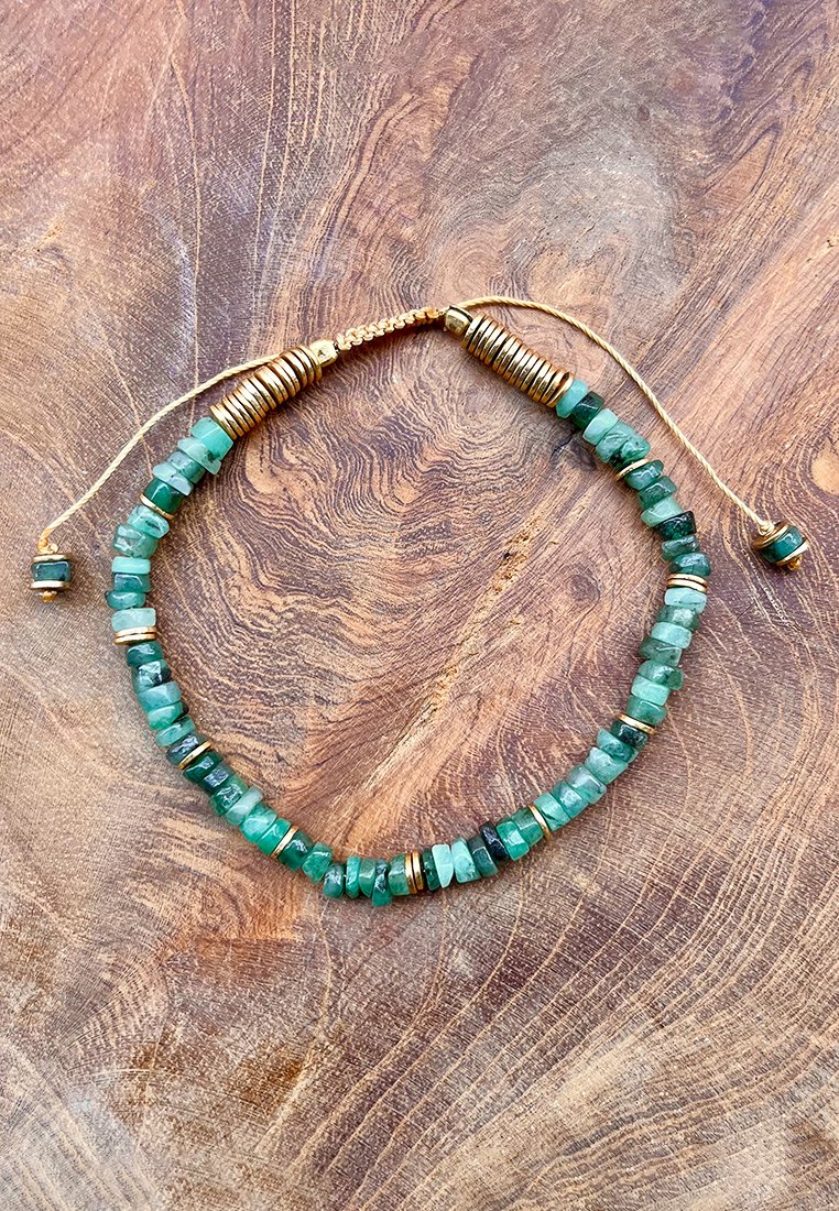 Collana di perline con gemme verdi, separatori in metallo dorato, texture liscia e forme variabili. Finitura con chiusura a cordino.