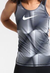 Débardeur de sport rayé noir et blanc avec un col rond et le logo Nike sur la poitrine ; coupe ajustée et tissu extensible.