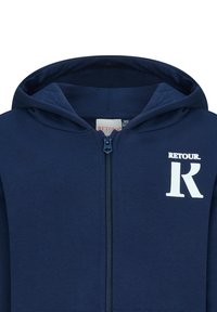 Marineblauwe zip-up hoodie van zachte stof, met een wit "RETOUR" logo en een grote witte letter "R" op de linkerborst. Gladde textuur, kangoeroezak.