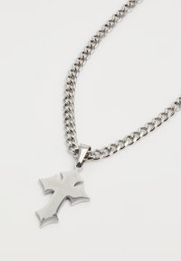 Silver chain necklace featuring a large metallic cross pendant with a polished finish and detailed edges, resting against a white background.