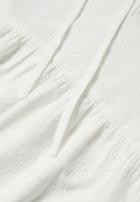 Witte katoen stof met een getextureerd bloemenpatroon en subtiele stiksels, wat zorgt voor een zachte, gelaagde uitstraling en een ontspannen pasvorm.